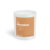 White cylindrical candle with tan label reading "I AM Abundant" and scent notes including pink pepper, saffron, cardamom, and