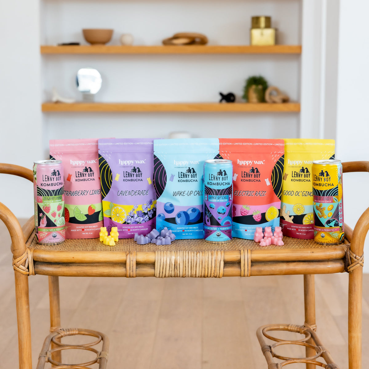 Five colorful kombucha bottles with fruit-themed labels and matching colored candies arranged on a wooden bench.