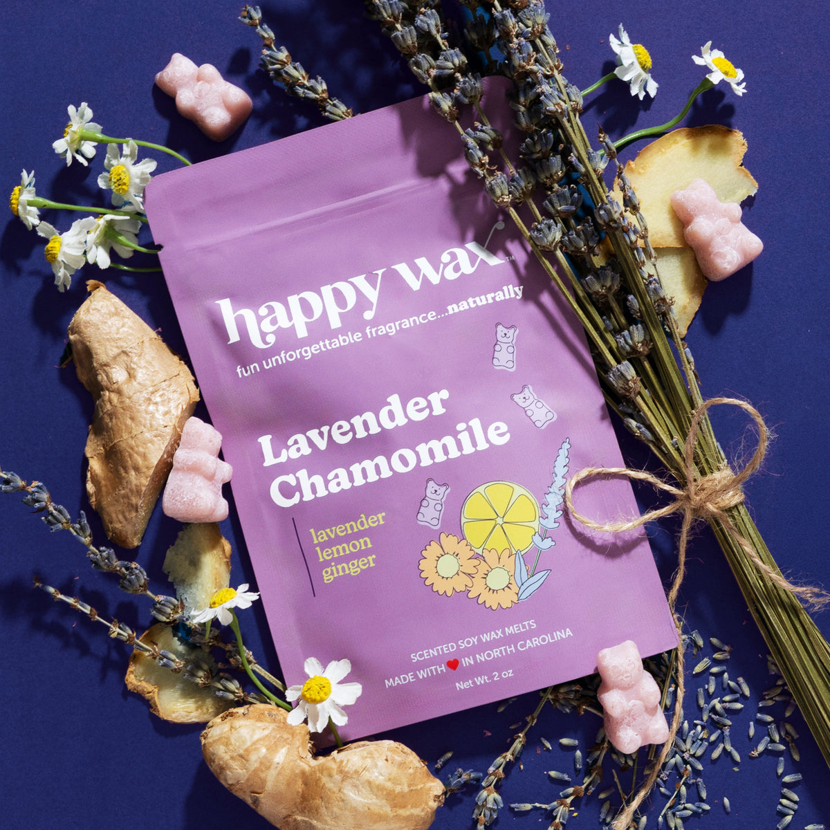 Purple pouch of lavender chamomile wax melts surrounded by dried flowers, ginger root, lemon slices, and pink wax melts on bl