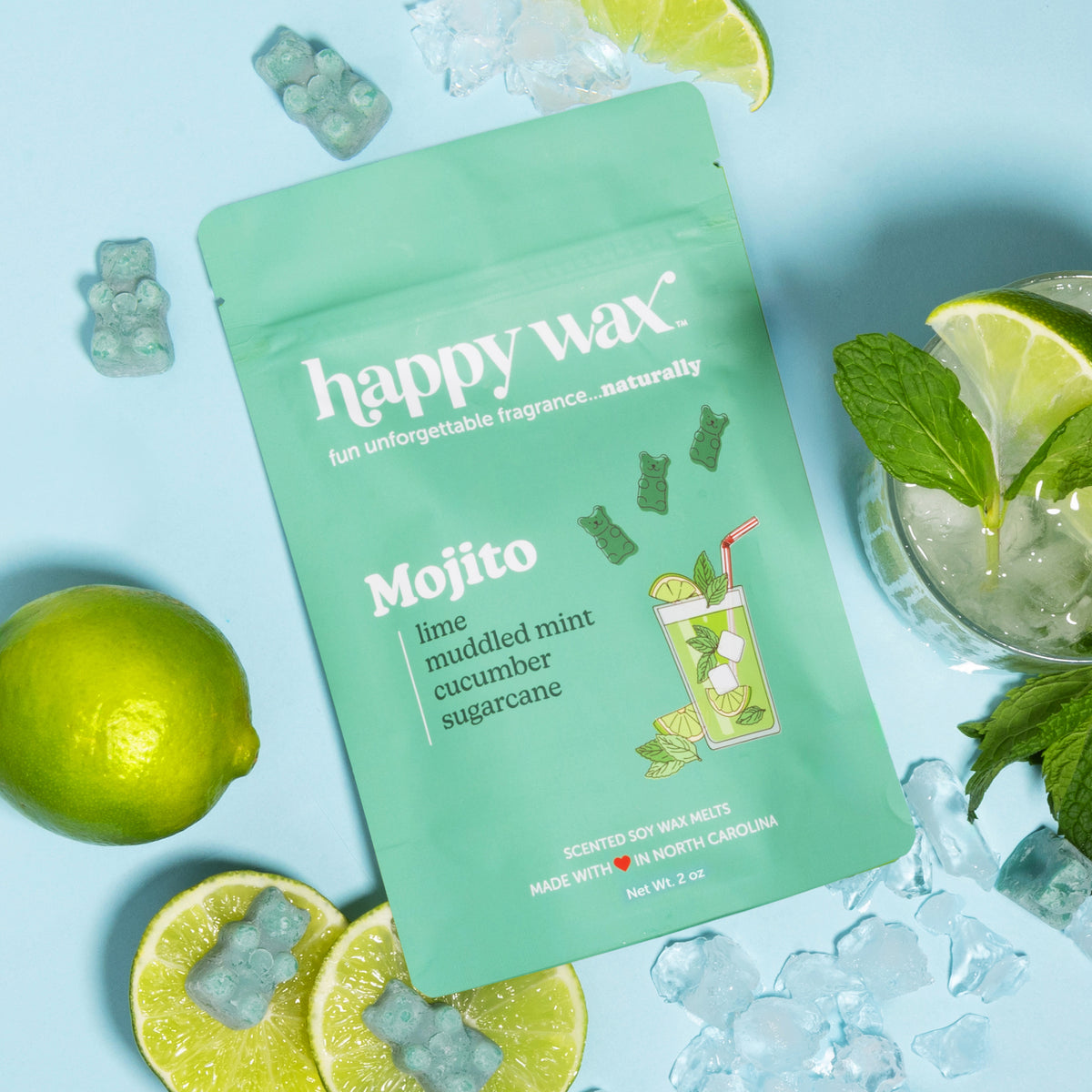 Green "happy wax" Mojito wax melt package surrounded by fresh limes, mint, ice cubes, and a mojito cocktail.