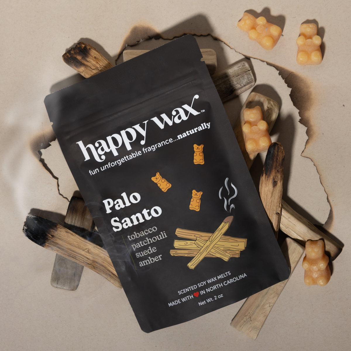 Black Happy Wax pouch of Palo Santo wax melts surrounded by tan-colored wax pieces and dried wood sticks.