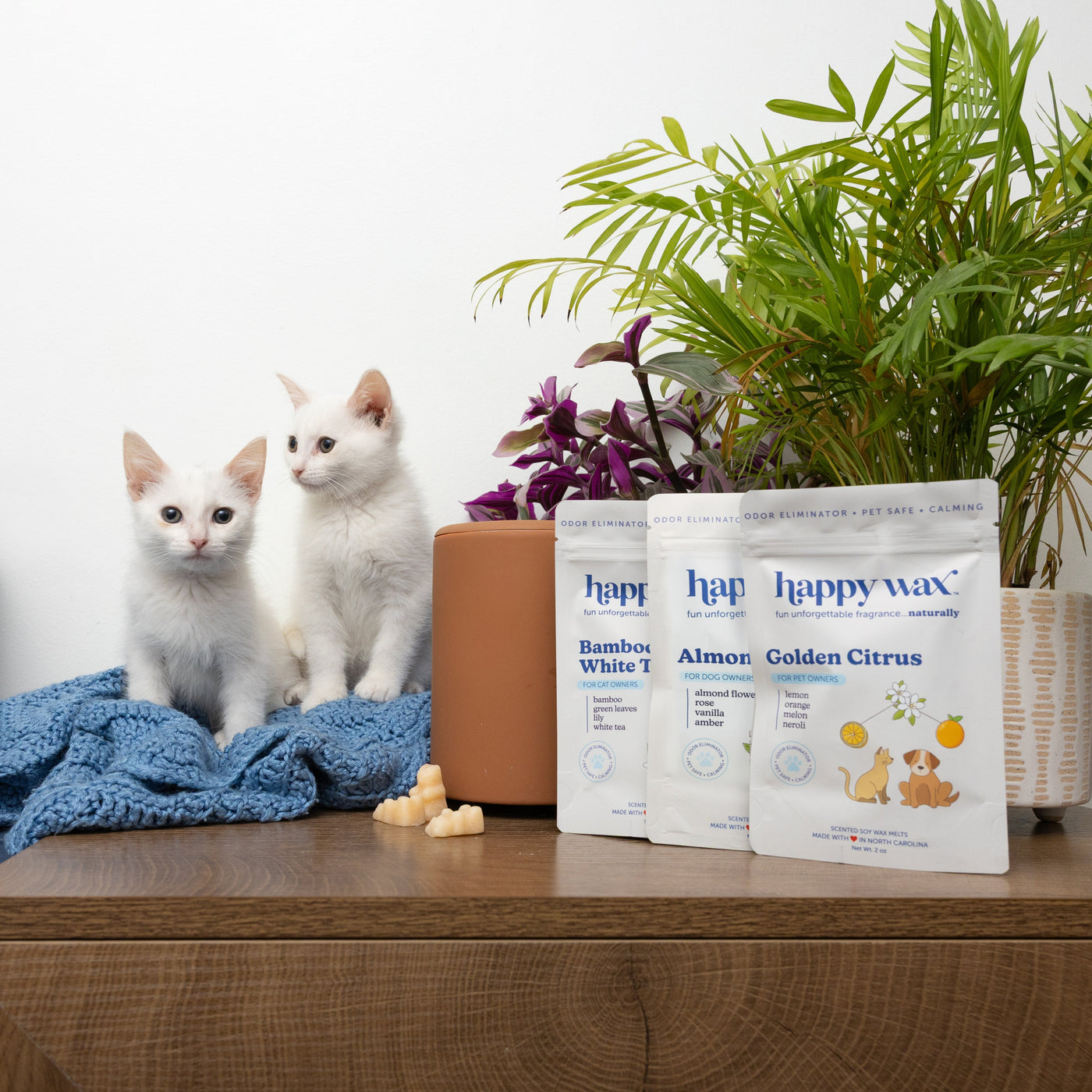 Three white pouches labeled "happy wax" with scents Bamboo White Tea, Almond, and Golden Citrus displayed next to two white c