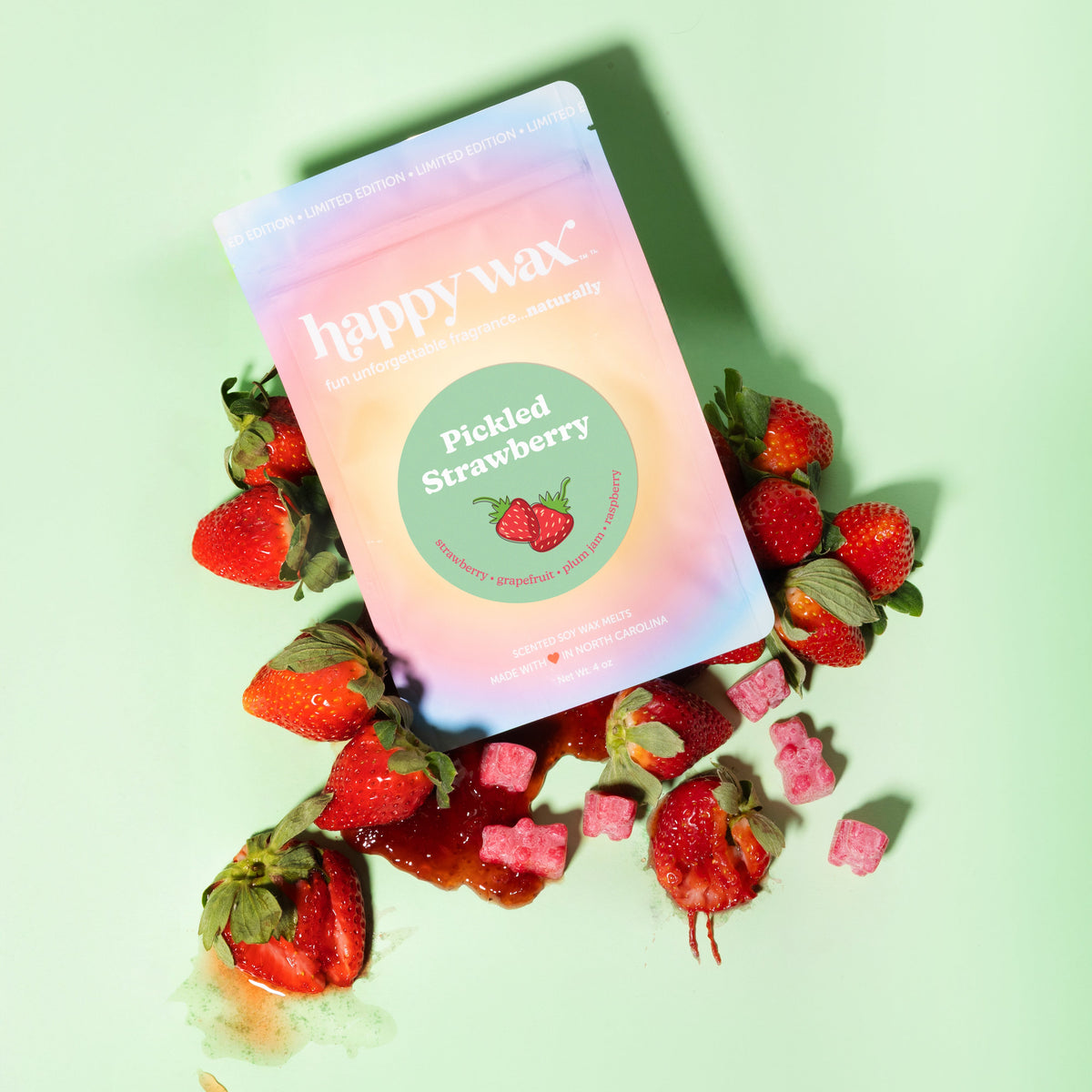 Happy Wax Pickled Strawberry wax melts in gradient packaging surrounded by fresh strawberries and pink wax pieces.