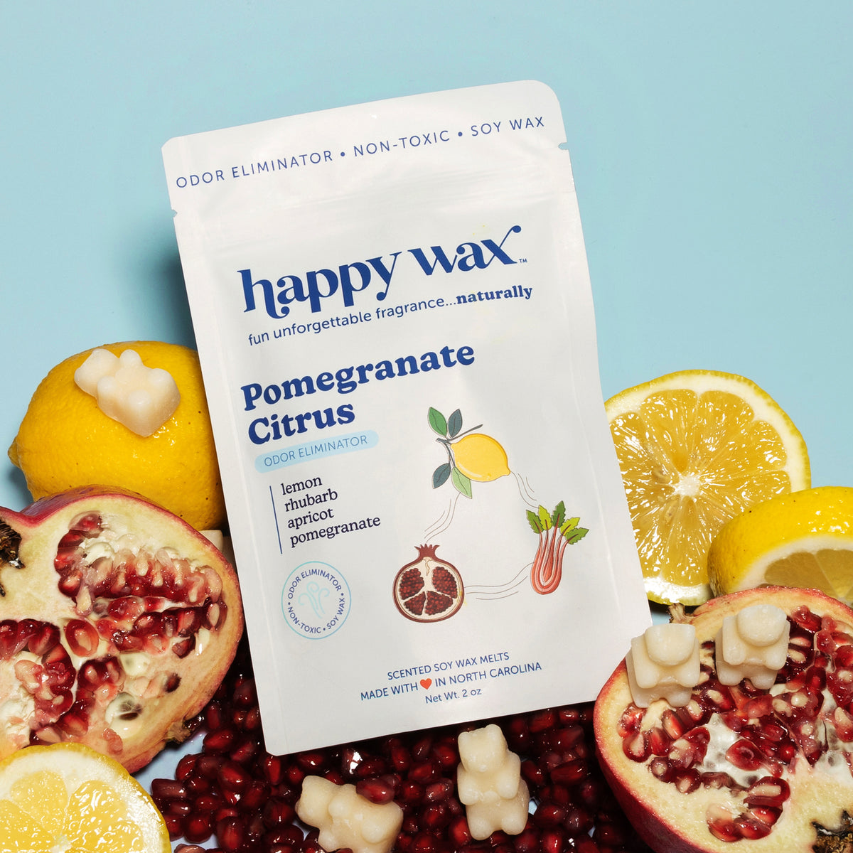 White pouch of Happy Wax pomegranate citrus soy wax melts surrounded by fresh pomegranates, lemon slices, and wax melt pieces