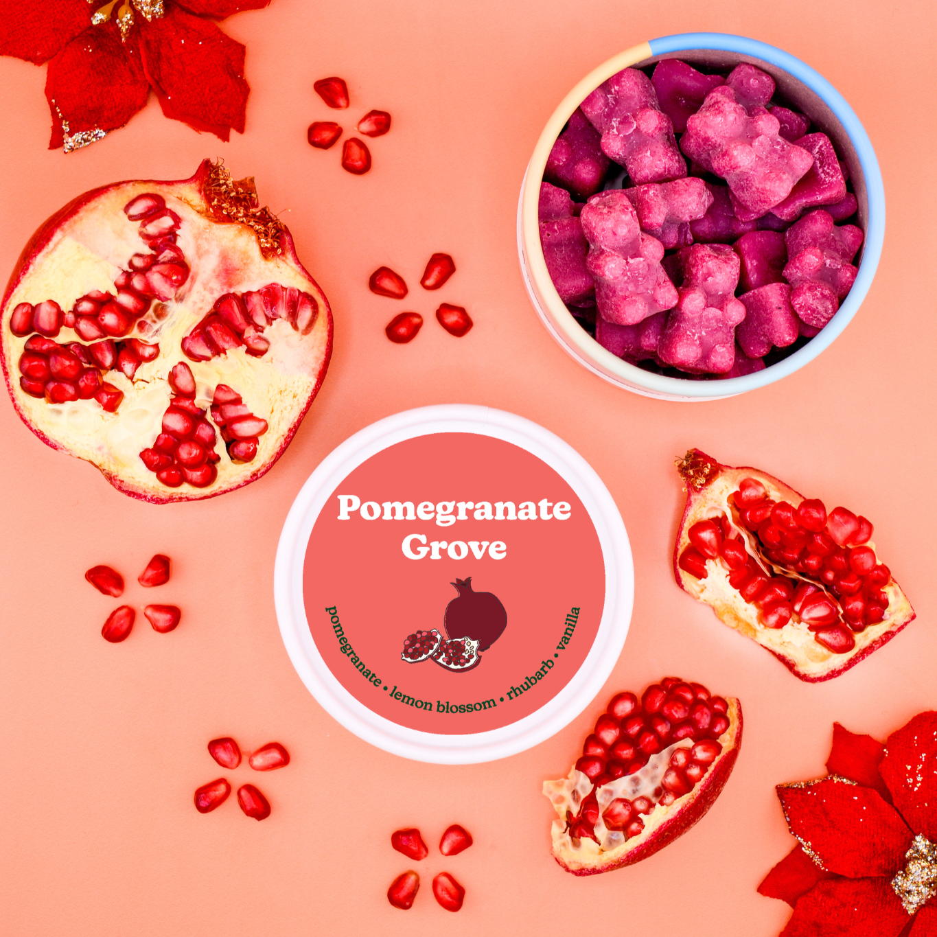 Magenta wax melts in blue-rimmed bowl surrounded by pomegranate halves, seeds, and red flowers on coral background.