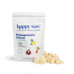 Cream-colored wax melts next to white pouch labeled "happy wax Pomegranate Citrus" with lemon, pomegranate, and rhubarb illus
