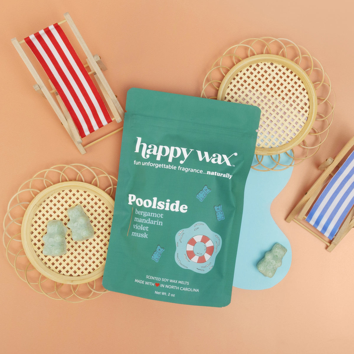 Green pouch of Poolside wax melts surrounded by striped beach chair, woven baskets, and scallop-shaped dishes on tan backgrou