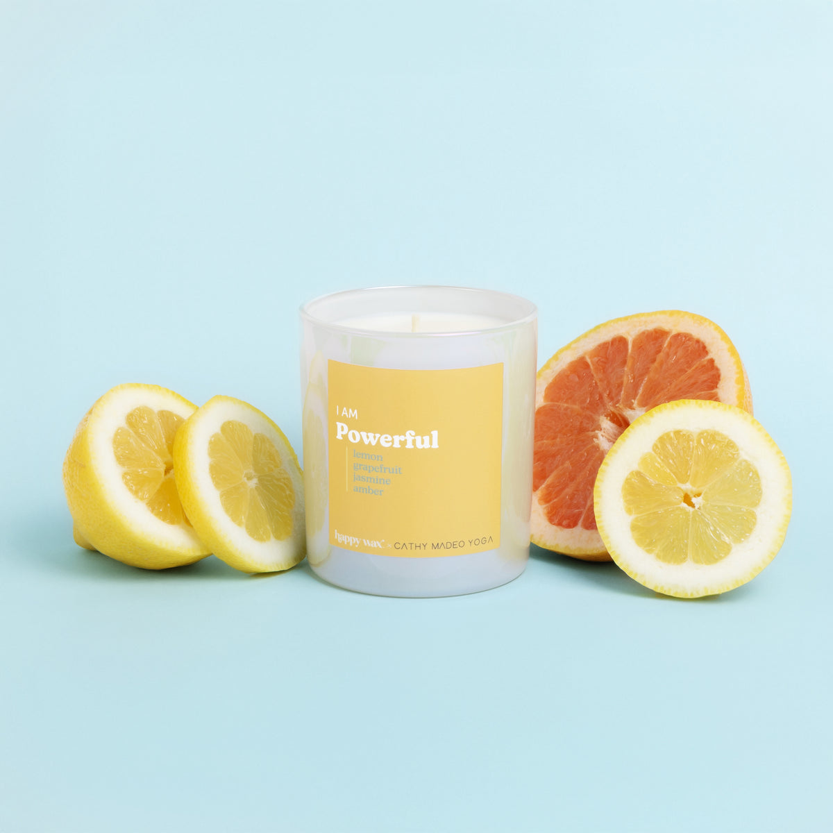 White cylindrical candle with yellow label reading "I AM Powerful" surrounded by fresh lemon and grapefruit halves on blue ba