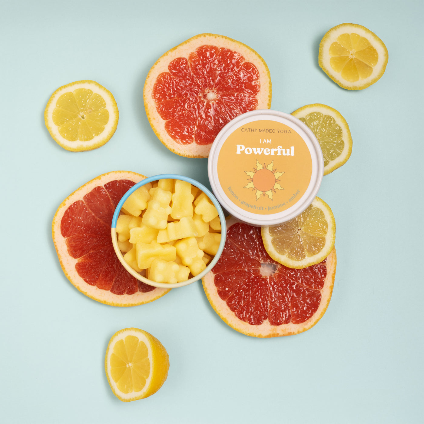 Container of yellow wax melts labeled "I am Powerful" surrounded by fresh grapefruit and lemon slices on light blue backgroun