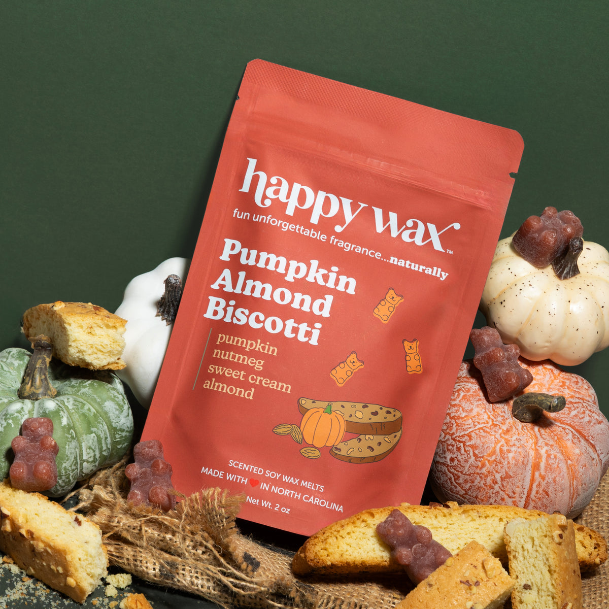 Happy Wax Pumpkin Almond Biscotti pouch with pumpkins, biscotti, brown wax bears and burlap fabric on dark green background