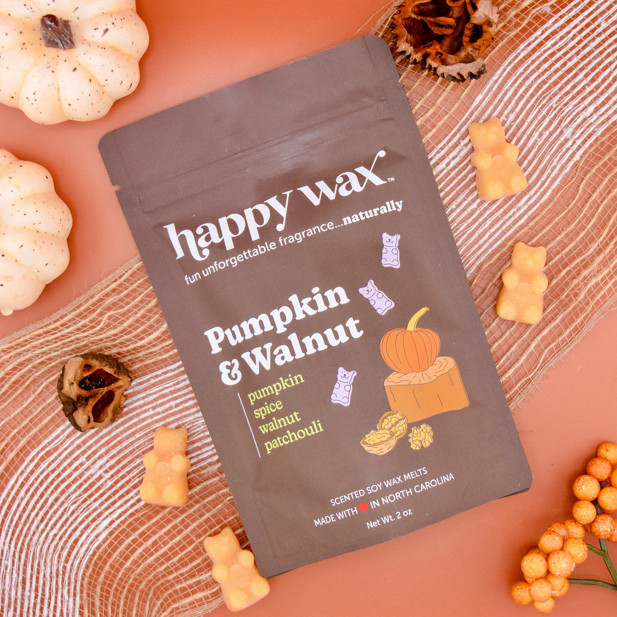 Brown pouch of pumpkin and walnut wax melts surrounded by yellow bear-shaped melts, decorative pumpkins, and dried botanicals