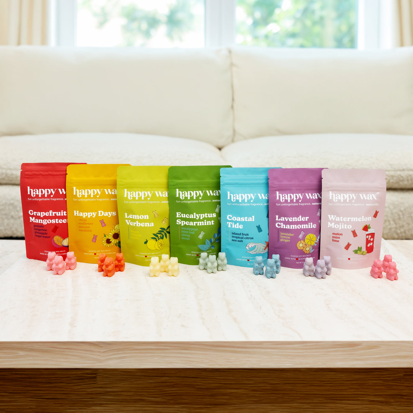 Seven Happy Wax scent pouches in rainbow colors with matching wax melts displayed on a white bed.