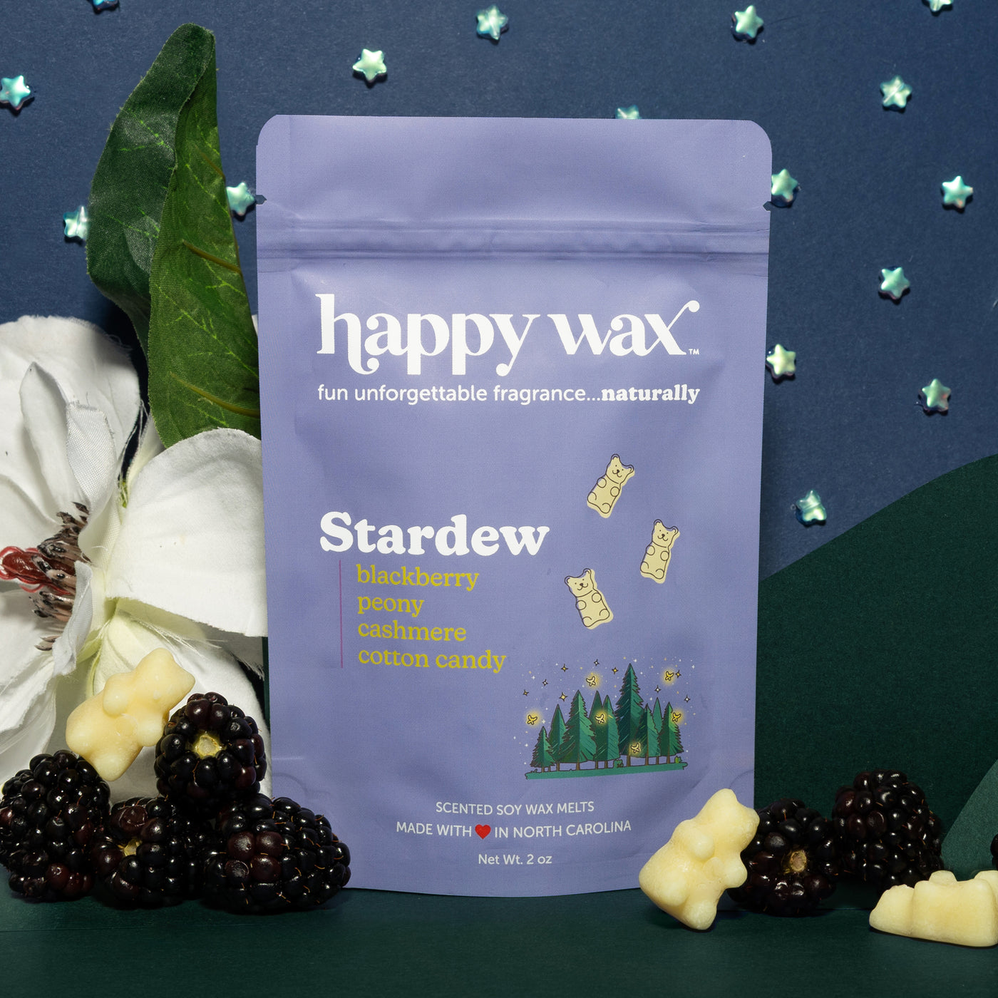 Purple pouch of Happy Wax Stardew scented soy wax melts surrounded by blackberries, white flowers, and decorative star shapes