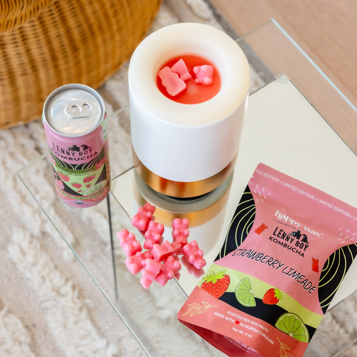 White wax melt warmer with gold band filled with red wax and pink shaped melts, surrounded by loose pink wax pieces and produ