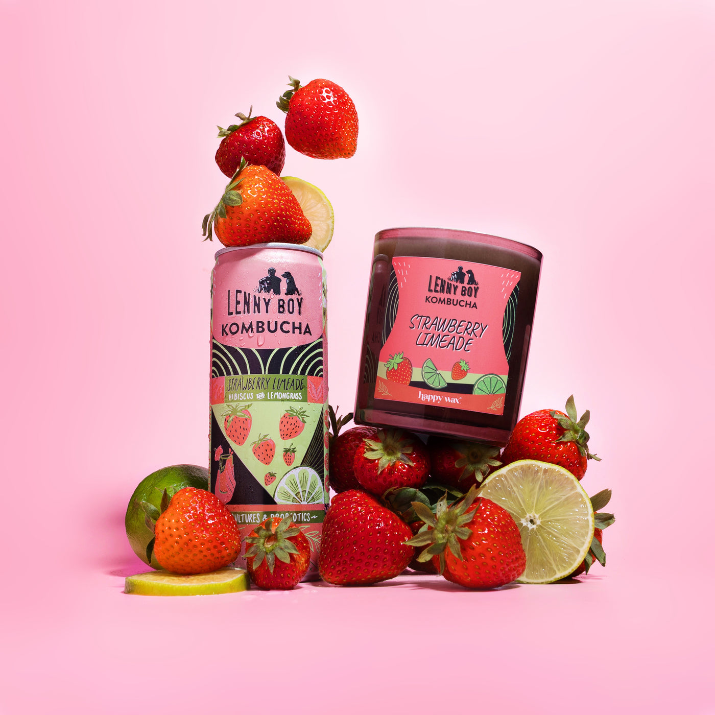 Pink glass candle jar with "Strawberry Limeade" label surrounded by fresh strawberries and lime slices on pink background.
