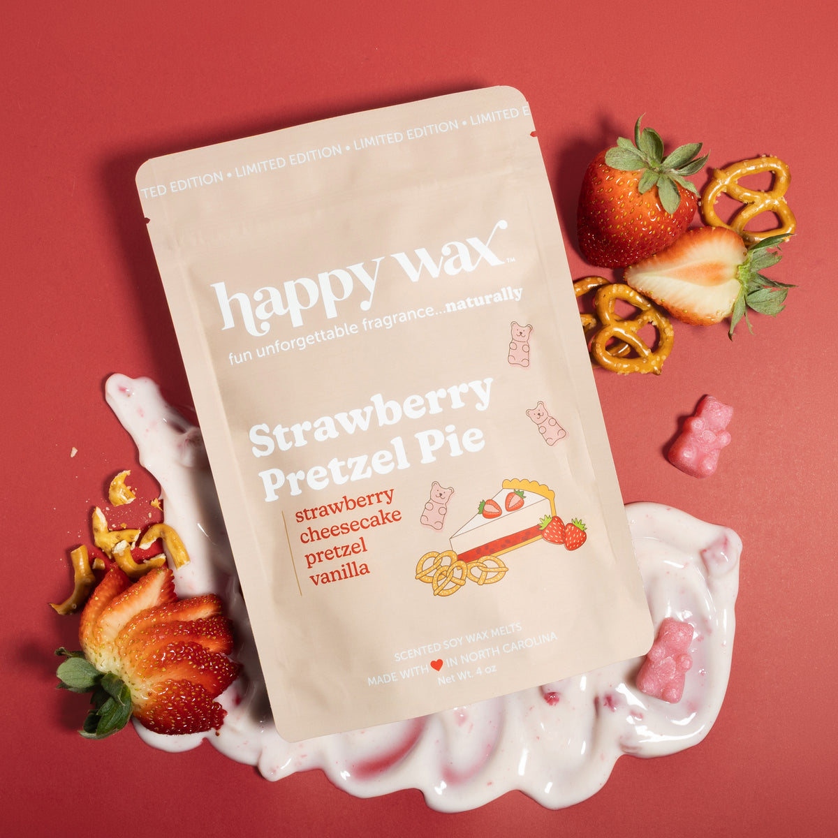 Cream pouch of Strawberry Pretzel Pie wax melts surrounded by fresh strawberries, pretzel pieces, and pink wax melts on red b
