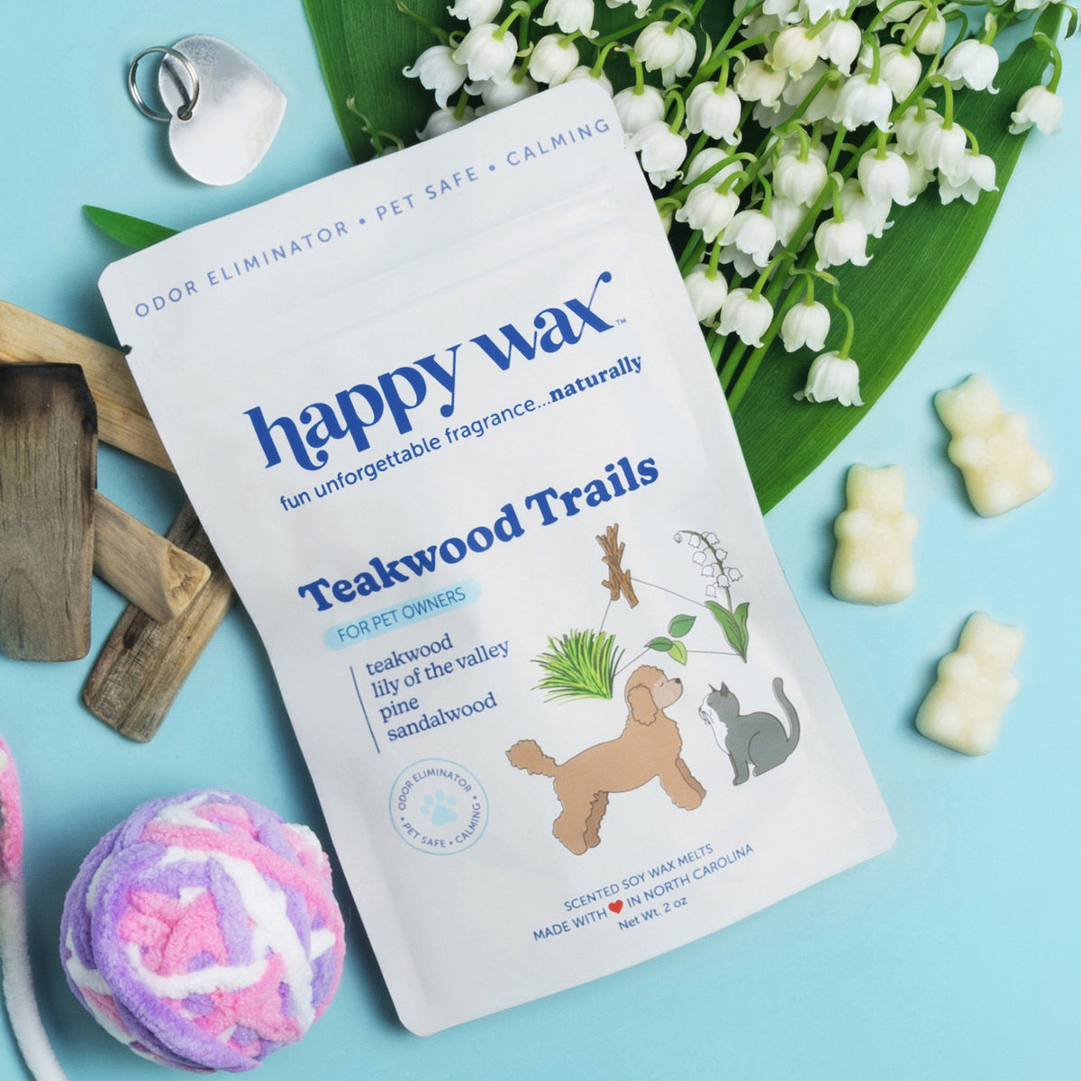 Happy Wax Teakwood Trails pet wax melts package with cream-colored wax melts, surrounded by white flowers, wooden blocks, and