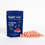 Navy blue pouch of Happy Wax Tropical Citrus wax melts with scattered pink wax cubes displayed beside it.