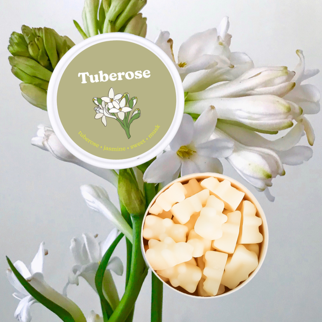 Cream-colored wax melts in white container next to olive-green labeled lid with tuberose flowers.