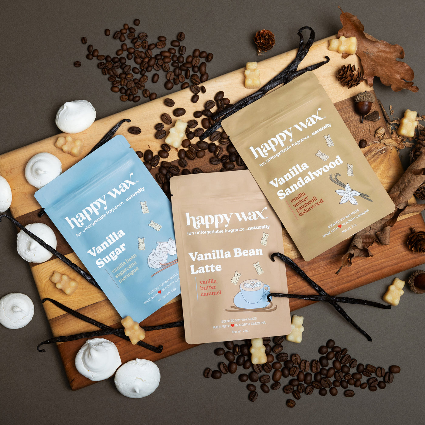 Three happy wax pouches labeled Vanilla Sugar, Vanilla Bean Latte, and Vanilla Sandalwood arranged with coffee beans, vanilla