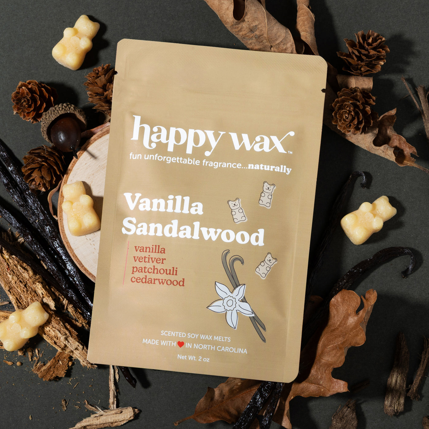 Tan pouch of Happy Wax Vanilla Sandalwood wax melts surrounded by cream-colored wax bear shapes, pinecones, vanilla pods, and