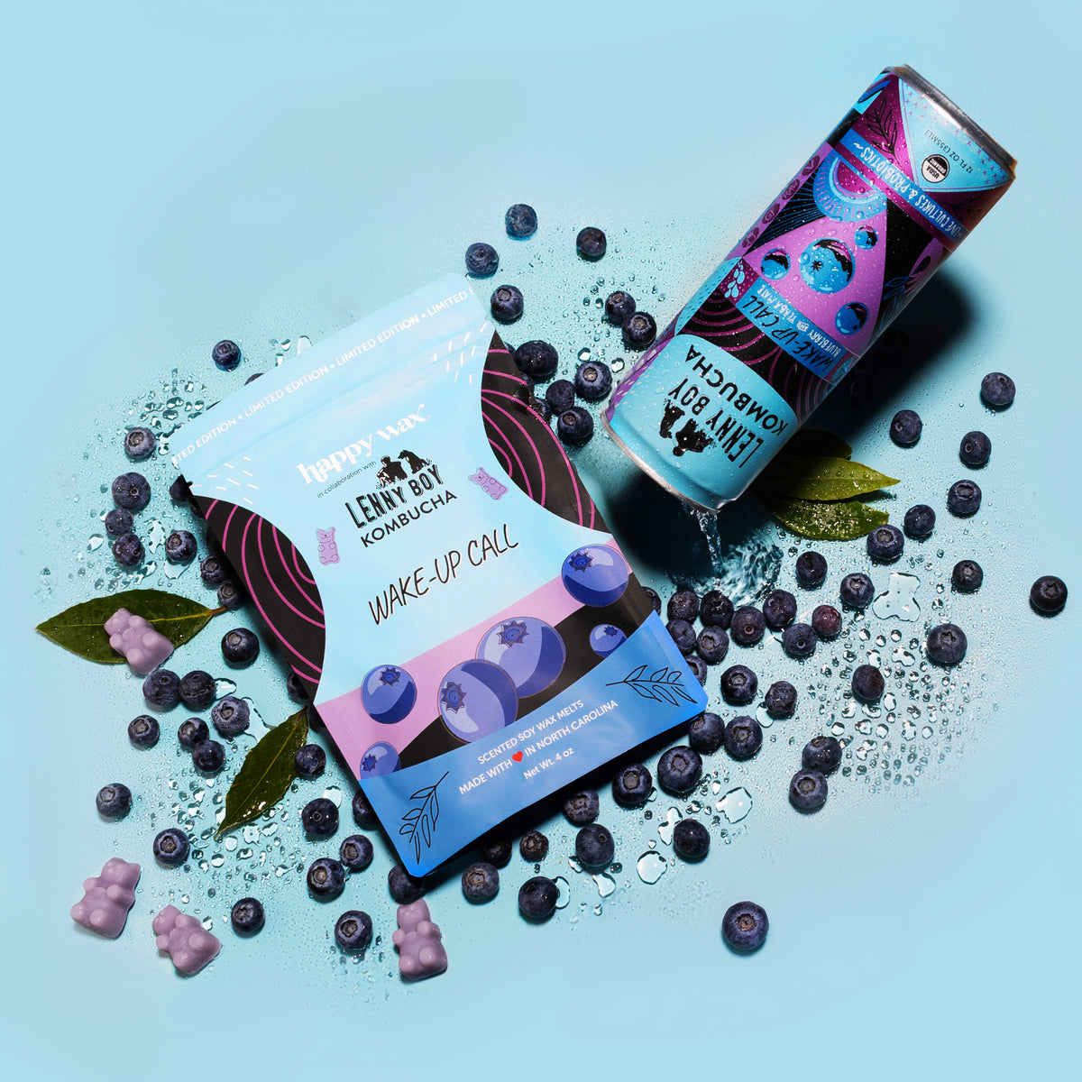 Two boxes of Wake Up Call wax melts with purple bear-shaped melts, fresh blueberries, and green leaves on a light blue backgr