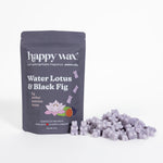 Purple wax melts scattered next to dark gray pouch labeled Water Lotus & Black Fig by happy wax.