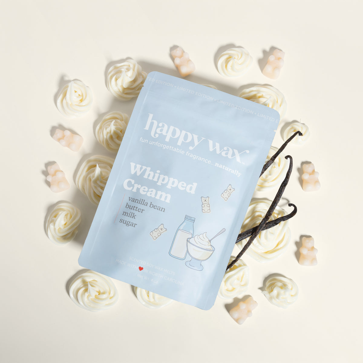 Light blue "happy wax" package of whipped cream wax melts surrounded by cream and gold swirled wax pieces and vanilla beans.