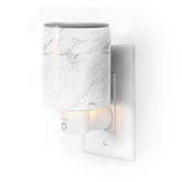 White marble-textured wax warmer with heating element, outlet plug, and control button mounted on wall plate.